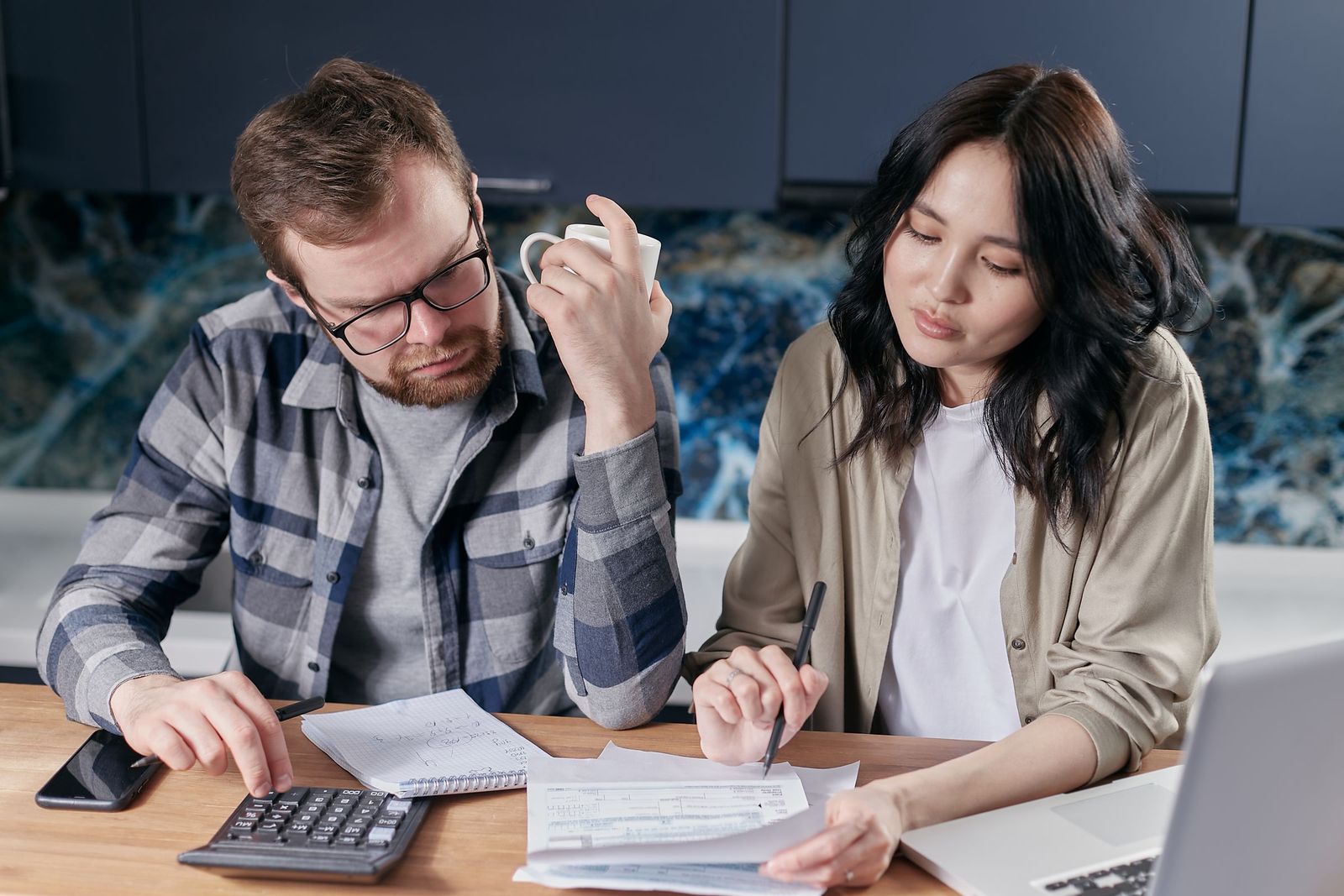 A couple at their kitchen table going through household bills with a laptop and calculator, sorting out council tax before moving house.