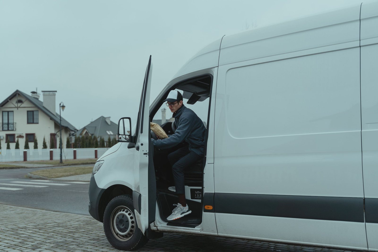 Courier stepping out of a white van with a parcel on a residential street